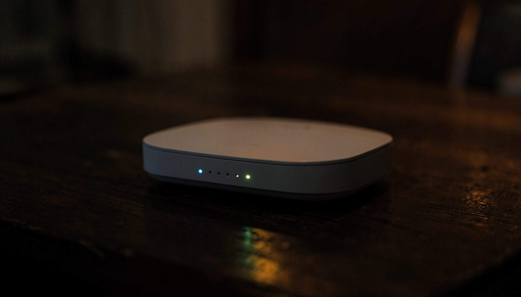 Router nirkabel dengan lampu indikator menyala di atas meja kayu gelap, suasana ruangan redup dengan cahaya hangat